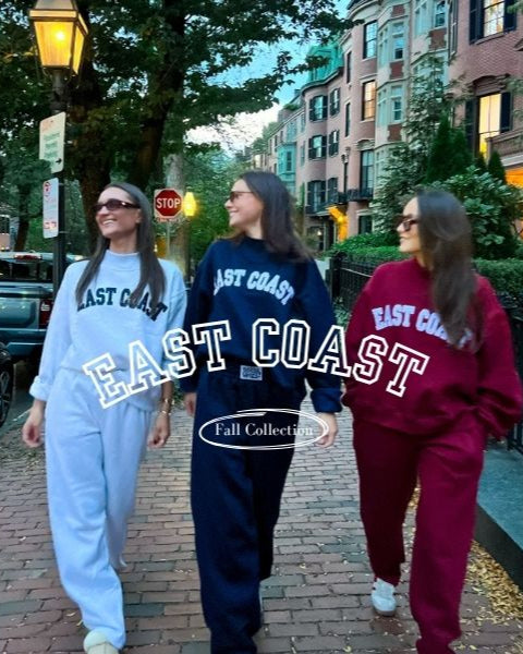 Three people wearing 'East Coast' themed sweatshirts walking on a street.
